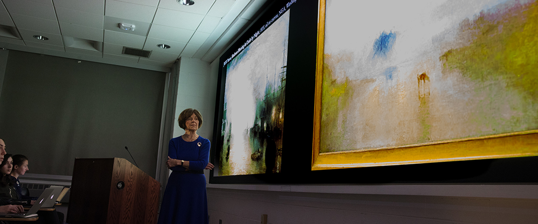 Professor lecturing class while looking at art on screen
