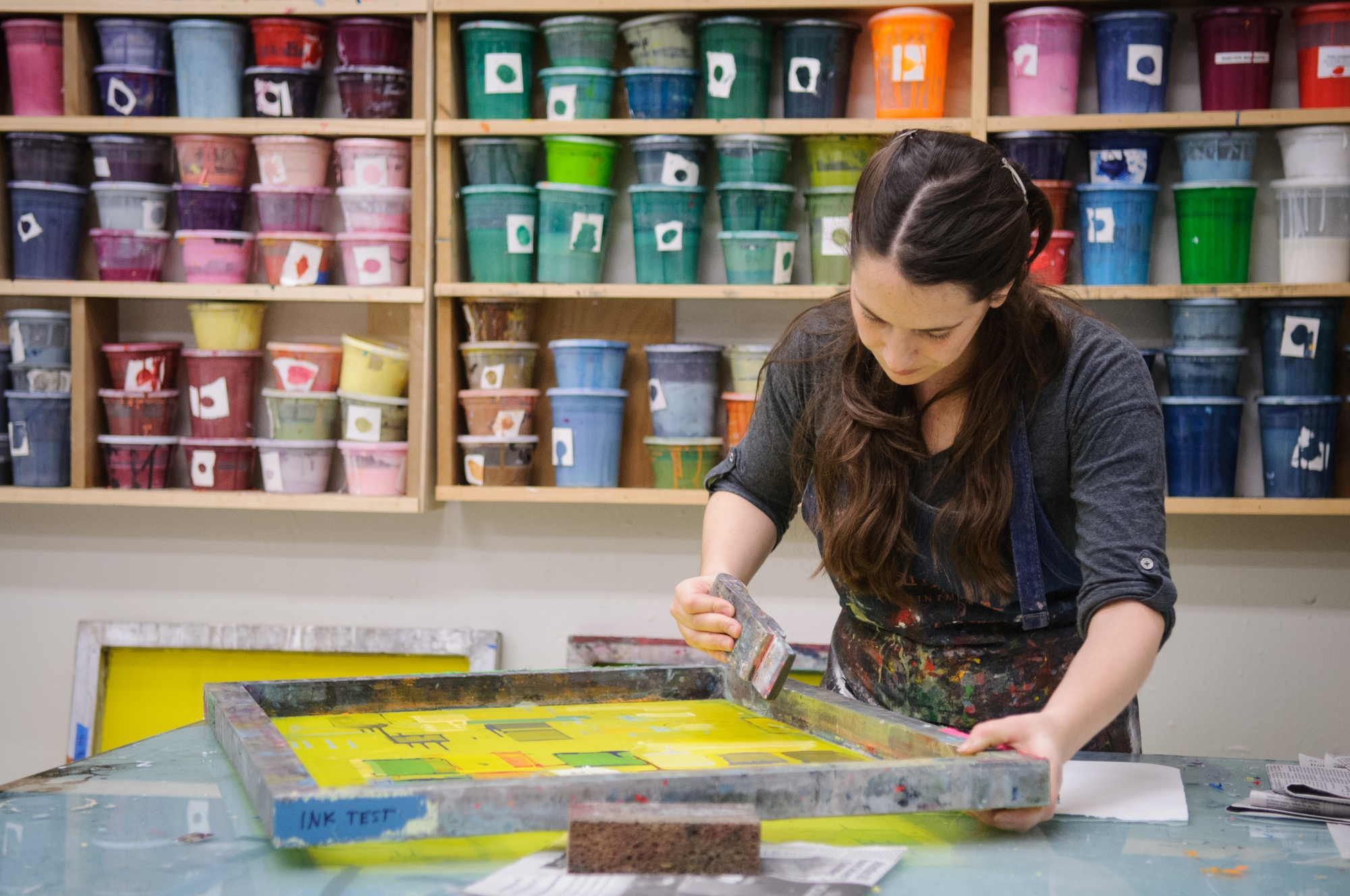 Student working on a painting in front of buckets of paint of many colors